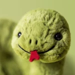 Close-up shot of Jellycat Stevie Snake’s soft sage green plush face, showing embroidered nostrils, a stitched smile, and a velvety red tongue.