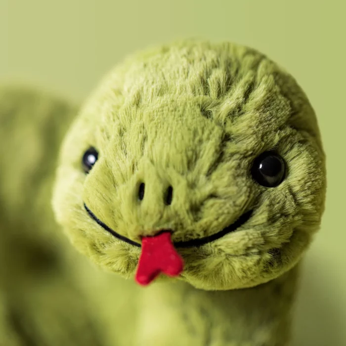 Close-up shot of Jellycat Stevie Snake’s soft sage green plush face, showing embroidered nostrils, a stitched smile, and a velvety red tongue.