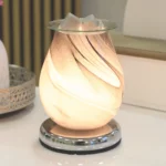 Grey Swirl Oval Aroma Electric Wax Melt Burner softly illuminated, showcasing its glowing grey swirl glass design, creating a warm and inviting ambiance in a stylish room setting.