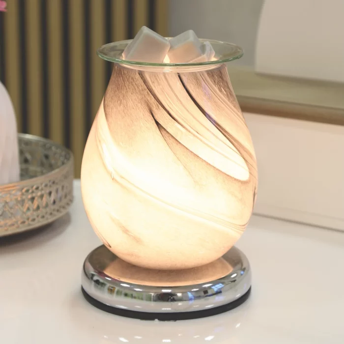 Grey Swirl Oval Aroma Electric Wax Melt Burner softly illuminated, showcasing its glowing grey swirl glass design, creating a warm and inviting ambiance in a stylish room setting.