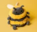 Jellycat Albee Bee plush toy with fluffy yellow and black stripes, smiling on a matching yellow background.