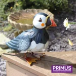 The large Puffin Metal Garden Ornament shown on a wooden ledge beside a birdbath and garden flower.