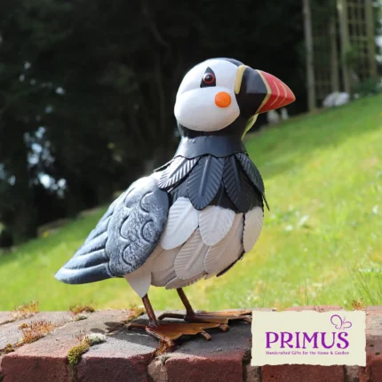 The large Puffin Metal Garden Ornament displayed on a brick wall in a grassy outdoor setting.