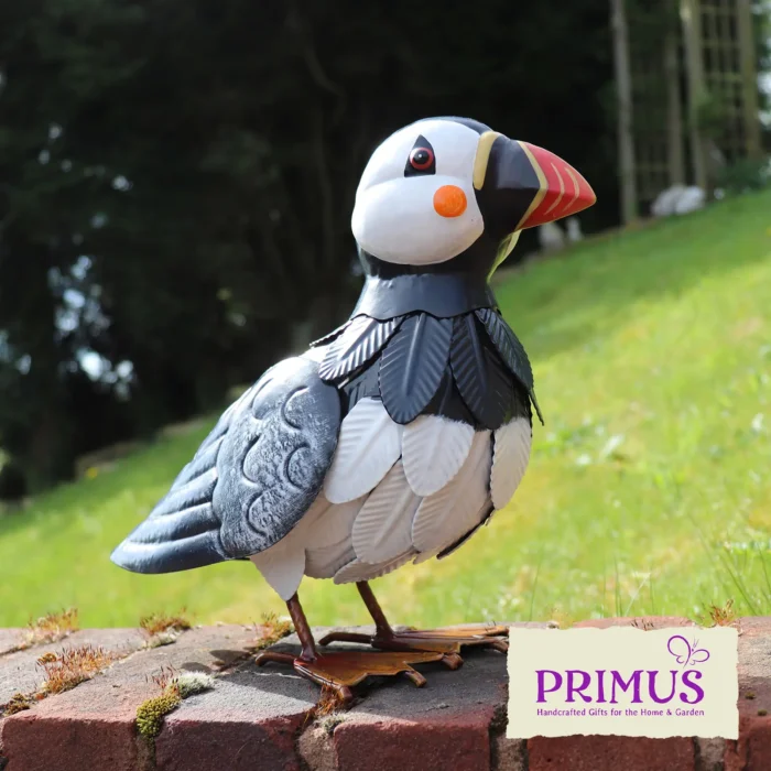 The large Puffin Metal Garden Ornament displayed on a brick wall in a grassy outdoor setting.