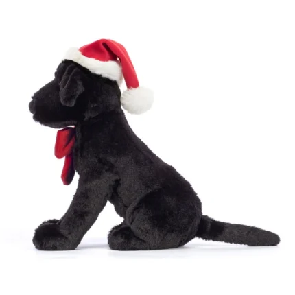 Side view of Jellycat Winter Warmer Pippa Labrador, showing the festive red bow, floppy ear, and sitting pose.