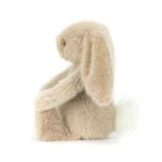 Side view of Jellycat Oat Flufflet Bunny showing plush oat beige fur, long floppy ear and fluffy cream tail.